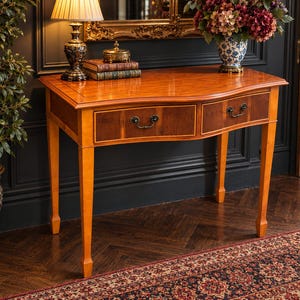 May include: A wooden console table featuring a curved front design with two drawers, each equipped with dark metal pull handles. The table has a light brown finish on the frame and legs, with darker wood veneer panels on the drawer fronts.