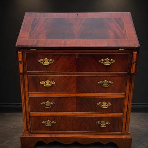 Peut inclure: Un secrétaire en acajou doté d'un abattant avec un motif de grain de bois riche, trois tiroirs inférieurs et un tiroir supérieur. Le meuble est orné de poignées pivotantes en laiton et d'entrées de serrure sur chaque tiroir.
