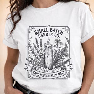 Könnte beinhalten: Weißes T-Shirt mit einer schwarz-weißen Grafik einer Kerze, umgeben von botanischen Illustrationen. Der Text auf dem Shirt lautet "SMALL BATCH CANDLE CO." und "HAND POURED • SLOW MADE".