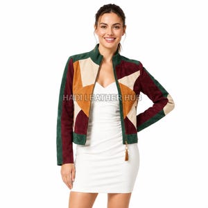 Puede incluir: Una chaqueta de ante multicolor con un patrón geométrico de estrellas en tonos verde oscuro, burdeos, tostado y crema. La chaqueta tiene cuello alto, cremallera frontal completa con un tirador de borla y el texto HADI LEATHER HUB impreso.