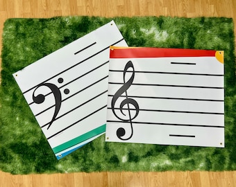 Könnte beinhalten: Zwei große weiße Notenlinien-Poster mit schwarzen Linien und musikalischen Symbolen, einem Bassschlüssel und einem Violinschlüssel. Ein Poster hat einen roten oberen Rand, das andere einen grünen und blauen unteren Rand. Sie liegen auf einem grünen Shag-Teppich.