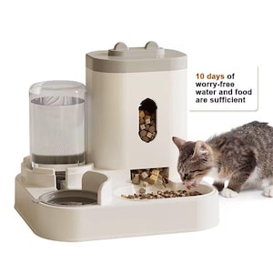 May include: An automatic pet feeder with a water dispenser and food storage. The feeder is off-white with a grey top and ear-shaped accents. The text reads "10 days of worry-free water and food are sufficient." A cat is eating from the feeder.