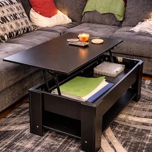 May include: A black lift-top coffee table with a raised tabletop revealing storage space. The table is rectangular and sits on a patterned rug. A candle and coasters are on the tabletop. The table is 40 inches long, 20 inches wide, and 18 inches high.