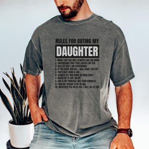 May include: A gray t-shirt with the text "RULES FOR DATING MY DAUGHTER" in a bold, black font. The text is centered and lists ten rules. The shirt is worn by a person.