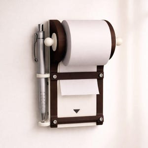 Könnte beinhalten: Ein dunkelbrauner, an der Wand befestigter Notizblock- und Papiertuchhalter mit einem silbernen Stift. Der Halter hat eine weiße Papierhandtuchrolle und einen Notizblock mit einem nach unten zeigenden Pfeil. Der Stift wird in einem weißen Kunststoffhalter gehalten.