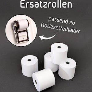 Könnte beinhalten: Weiße Papierrollen für einen Notizblockhalter. Das Bild zeigt mehrere Rollen weißes Papier, sowie eine Nahaufnahme eines Notizblockhalters mit einem Stift. Der Text im Bild lautet "Ersatzrollen" und "passend zu Notizzettelhalter".