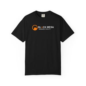 Könnte beinhalten: Schwarzes T-Shirt mit dem Logo "Black Mesa Research Facility" in Orange und Weiß. Das Logo zeigt einen orangefarbenen Kreis mit schwarzer Umrandung. Der Text "BLACK MESA" steht über "RESEARCH FACILITY".