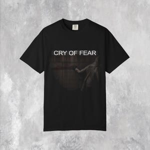 以下が含まれることがあります： 「CRY OF FEAR」の白文字が入った黒いTシャツ。 腕を伸ばす人物の暗く芸術的なグラフィックが特徴です。 Tシャツは、クラシックなクルーネックです。