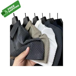 Pode incluir: Uma sele&ccedil;&atilde;o de camisas texturizadas com bot&otilde;es em v&aacute;rias cores, incluindo cinza, branco e azul marinho, penduradas em cabides pretos. As camisas t&ecirc;m um padr&atilde;o tecido. Um adesivo verde "FREE SHIPPING" est&aacute; no canto superior esquerdo.