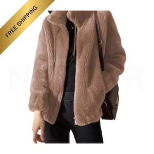 Puede incluir: Chaqueta de piel sintética marrón claro con cuello alto y cierre de cremallera. La chaqueta tiene mangas largas y se combina con pantalones negros. Se ve un pequeño bolso marrón.