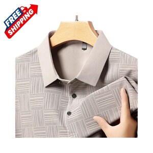 K&ouml;nnte beinhalten: Ein hellbeige Hemd mit Kragen und einem geometrischen Muster aus Quadraten und Linien. Das Hemd hat einen hellbeigen Kragen und zwei schwarze Kn&ouml;pfe. Das Hemd h&auml;ngt an einem Holzb&uuml;gel.