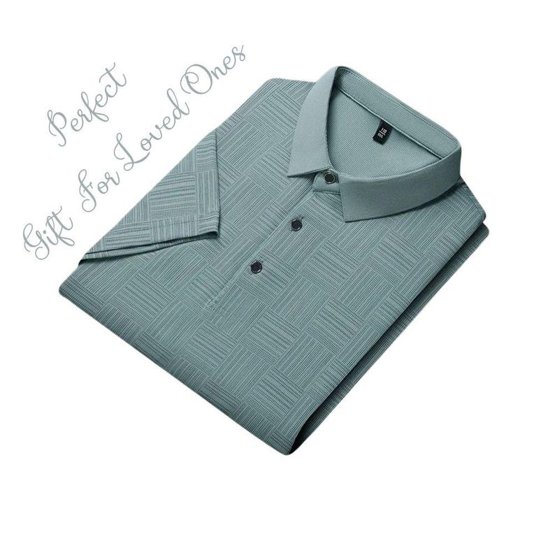 K&ouml;nnte beinhalten: Ein gefaltetes, helles tealfarbenes Poloshirt mit einem strukturierten, gitterartigen Muster. Das Hemd hat einen Kragen und drei dunkle Kn&ouml;pfe. Die Worte "Perfect Gift For Loved Ones" sind kursiv geschrieben.