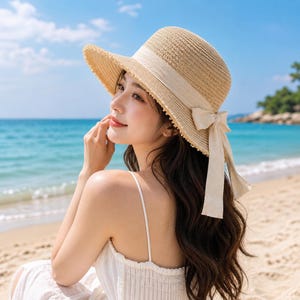 May include: A straw sun hat with a wide brim and a beige ribbon tied in a bow. The hat is light brown and has a textured weave. The hat is designed for sun protection and is suitable for beach or outdoor wear.