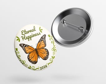May include: A round button with a monarch butterfly illustration and the words "Eternal Happiness 2026". The butterfly is orange and black, with a green floral border. A second, silver button is also visible.