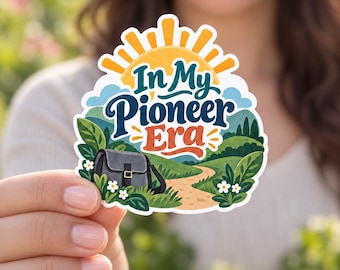 May include: A die-cut sticker featuring a yellow sun rising over green hills and a dirt path. The text In My Pioneer Era is written in dark blue and orange. A grey satchel bag sits in the foreground among green leaves and small white flowers.