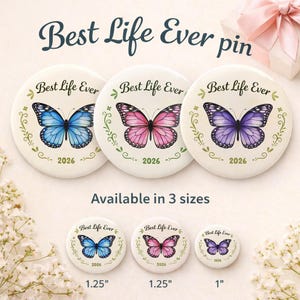 Puede incluir: Broches redondos blancos con diseños de mariposas en azul, rosa y morado, con el texto "Best Life Ever" y "2026". Los broches están disponibles en tres tamaños: 2,54 cm, y 3,18 cm.