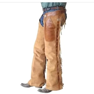 Puede incluir: Chaps de cuero color canela con un parche de cuero marrón en el muslo y flecos en los laterales. Los chaps se llevan sobre unos vaqueros azules y se combinan con botas de vaquero, mostrando un estilo western.
