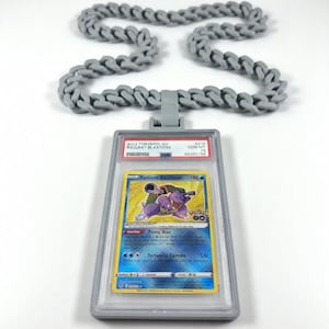 Może przedstawiać: Szary naszyjnik z wisiorkiem przedstawiającym kartę kolekcjonerską Pok&eacute;mon. Karta jest zamknięta w przezroczystym plastikowym uchwycie i wyświetla kartę Radiant Blastoise. Karta ma niebiesko-ż&oacute;łty design.