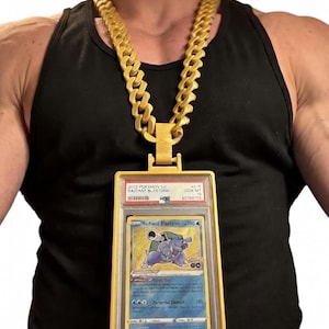 May include: A gold-coloured chain necklace with a large pendant. The pendant is a yellow frame holding a Pokémon card. The card features a blue turtle-like creature and the text "Radiant Blastoise". The necklace is worn over a black vest.