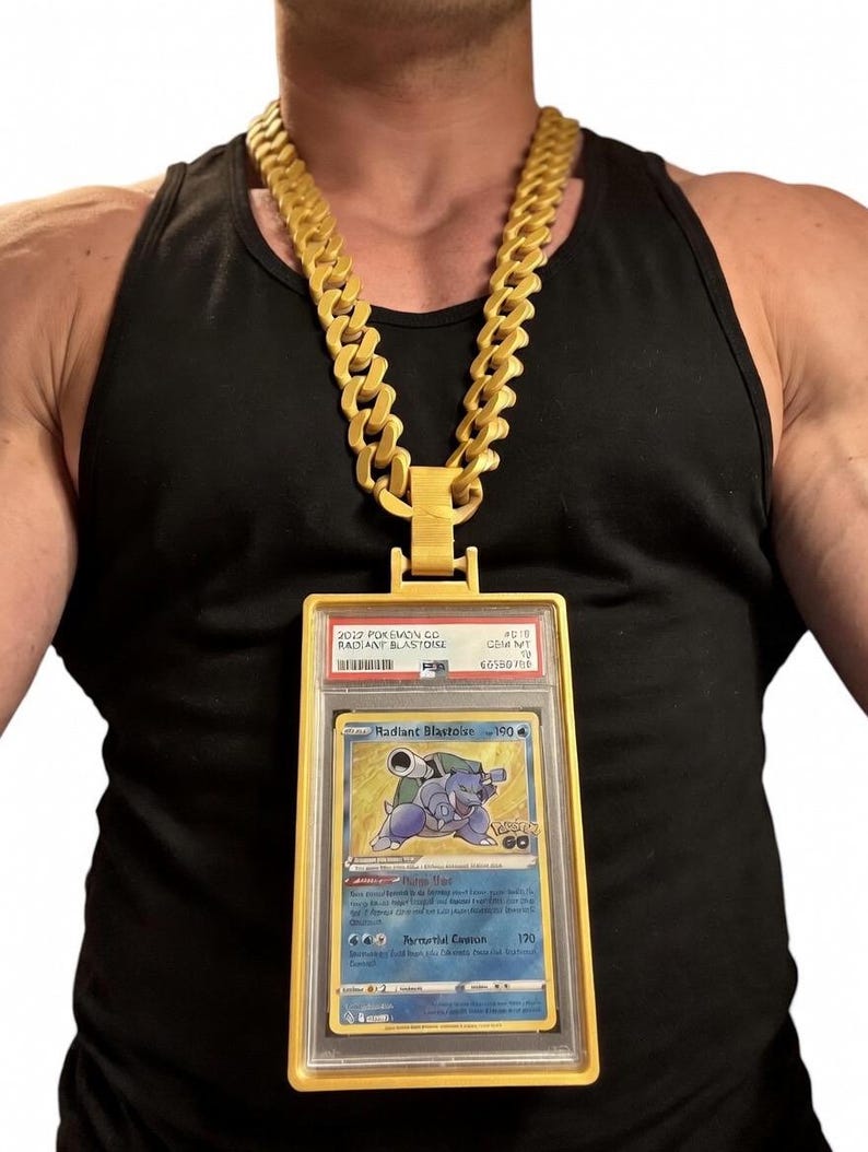 Puede incluir: Un collar de cadena gruesa de color dorado con un gran colgante de marco rectangular de color dorado que sostiene una tarjeta coleccionable Pokemon Radiant Blastoise 2022 graduada. La tarjeta muestra al personaje Blastoise con el texto Radiant Blastoise 190.
