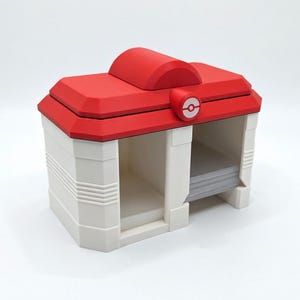 May include: A white and red storage container with a red roof and a circular emblem. The container has two open compartments and a small, rounded top. The design is reminiscent of a building.