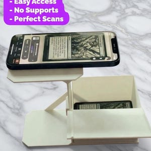 Puede incluir: Un soporte para teléfono de color crema con un teléfono que muestra una tarjeta. El soporte tiene un compartimento para una tarjeta. El texto en el soporte dice "Fast Print, Easy Access, No Supports, Perfect Scans."