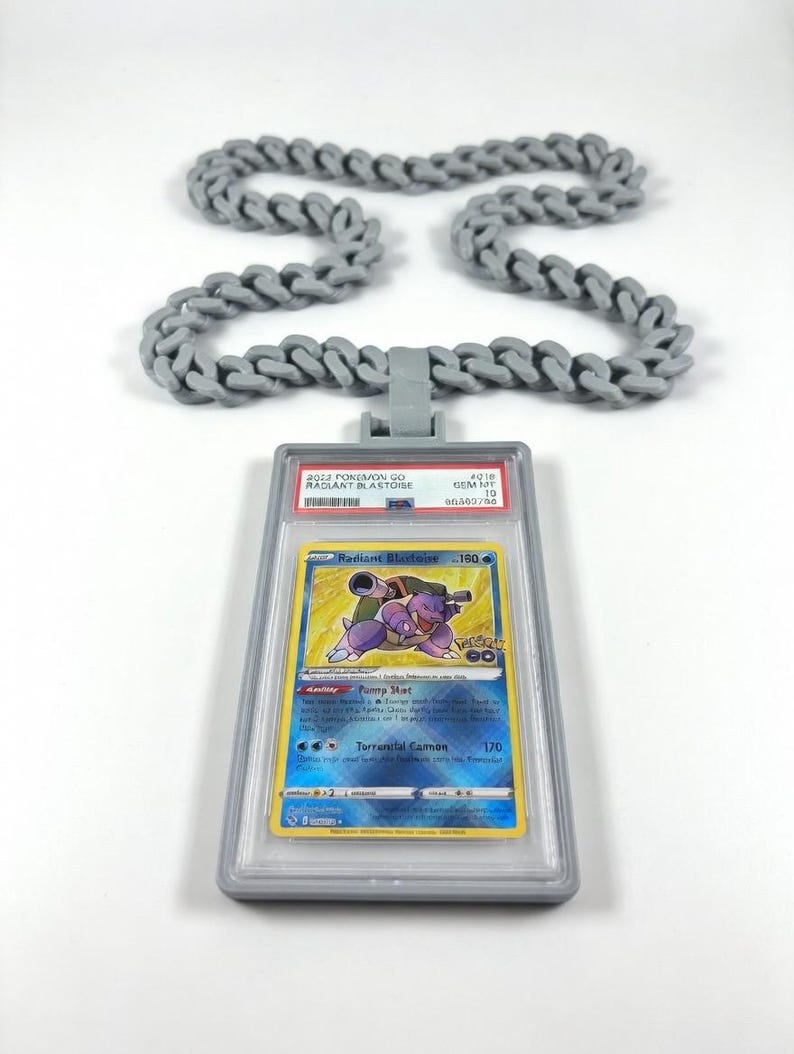 Puede incluir: Un collar de cadena de pl&aacute;stico gris con un colgante rectangular que contiene una tarjeta coleccionable 2022 Pokemon GO Radiant Blastoise graduada. La etiqueta de la tarjeta muestra el texto 2022 POKEMON GO RADIANT BLASTOISE GEM MT 10 80302700.