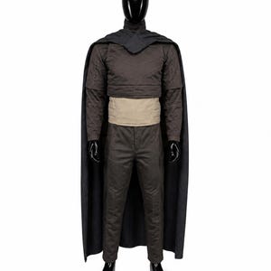 May include: A dark brown long-sleeved top with a high collar and chevron detailing, paired with matching dark brown trousers. A wide, light beige waist belt sits above the trousers. A long, dark gray cape drapes over the shoulders and back.