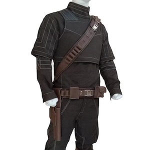 Op de afbeelding: Een zwarte set van een shirt met lange mouwen en een broek met witte contraststiksels, een hoge kraag en een bruine utility-riem in lederlook met holster, een schouderband met munitiegleuven en een bruin beenwikkel-accessoire.