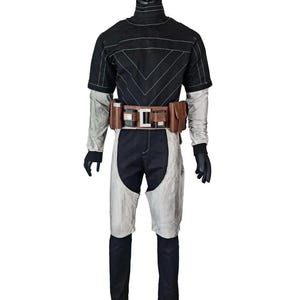 May include: A black and light gray jumpsuit featuring a high collar, short sleeves, and a fitted silhouette. The garment includes a brown utility belt with multiple pouches and a central metallic buckle, worn over the waist of the jumpsuit.