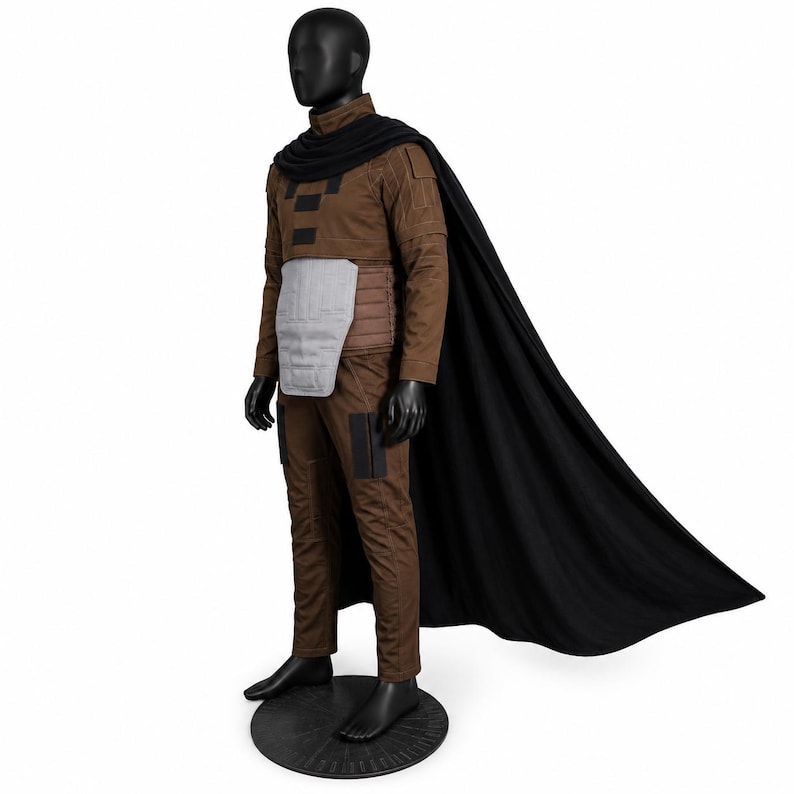 May include: A brown long-sleeved top and matching trousers set worn with a black cape. The outfit features a light gray chest plate, dark brown rectangular accents on the chest and thighs, and a brown ribbed waist section on a black mannequin.