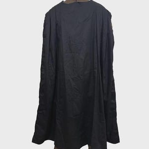 May include: A long, solid black cape with a smooth, matte texture. The garment features a high, structured collar that is brown with a visible vertical zipper closure at the center back. The cape hangs straight down in loose, vertical folds.