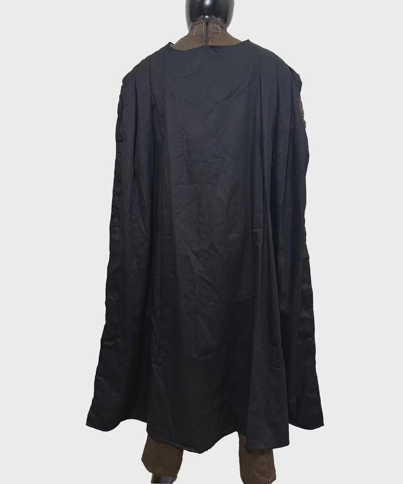 May include: A long, solid black cape with a smooth, matte texture. The garment features a high, structured collar that is brown with a visible vertical zipper closure at the center back. The cape hangs straight down in loose, vertical folds.