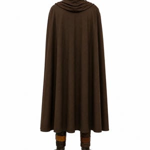 May include: A floor-length brown cloak featuring a hood with a gathered neckline and a smooth, solid-colored fabric. The garment hangs straight down, partially obscuring a pair of dark brown boots with tan straps visible at the bottom hem.