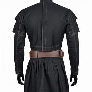 May include: A black cropped jacket with white topstitching, ribbed shoulder detailing, and long sleeves, paired with a brown utility belt featuring vertical slots and a black skirt. The jacket has a central vertical seam and a structured fit.