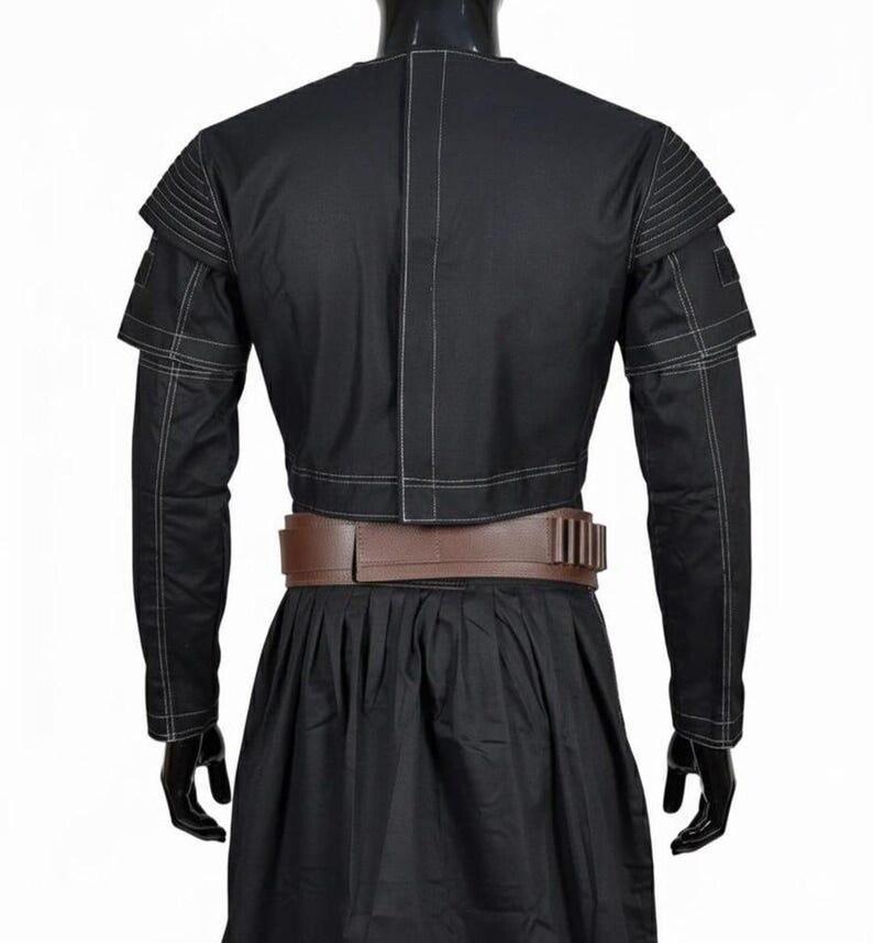May include: A black cropped jacket with white topstitching, ribbed shoulder detailing, and long sleeves, paired with a brown utility belt featuring vertical slots and a black skirt. The jacket has a central vertical seam and a structured fit.