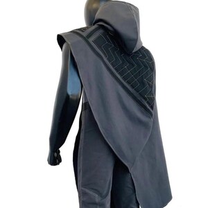 May include: A dark gray hooded cape featuring a geometric quilted pattern on the back panel with black trim accents. The cape is worn over matching dark gray trousers that have visible light-colored stitching along the seams and leg sections.