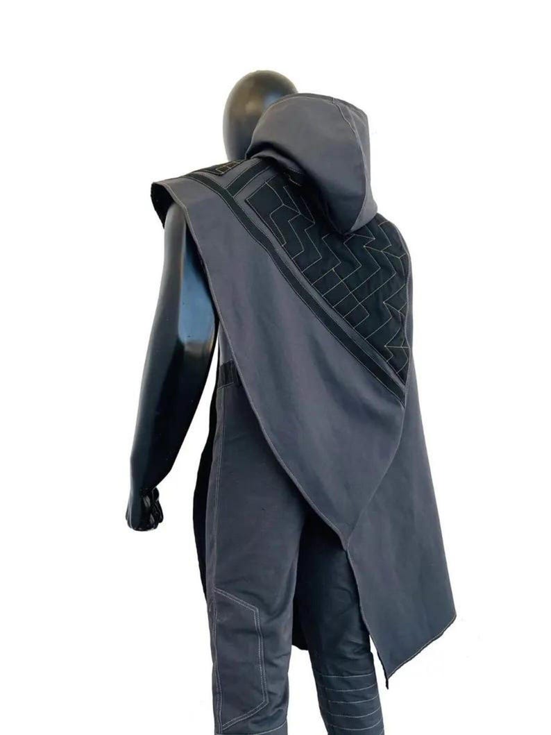 May include: A dark gray hooded cape featuring a geometric quilted pattern on the back panel with black trim accents. The cape is worn over matching dark gray trousers that have visible light-colored stitching along the seams and leg sections.