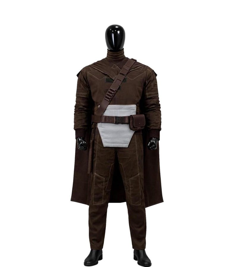 May include: A dark brown costume set on a mannequin, featuring a long-sleeved top, matching trousers, and a cape. The outfit includes a light gray rectangular abdominal panel, a dark brown utility belt with a pouch, and a diagonal shoulder strap.