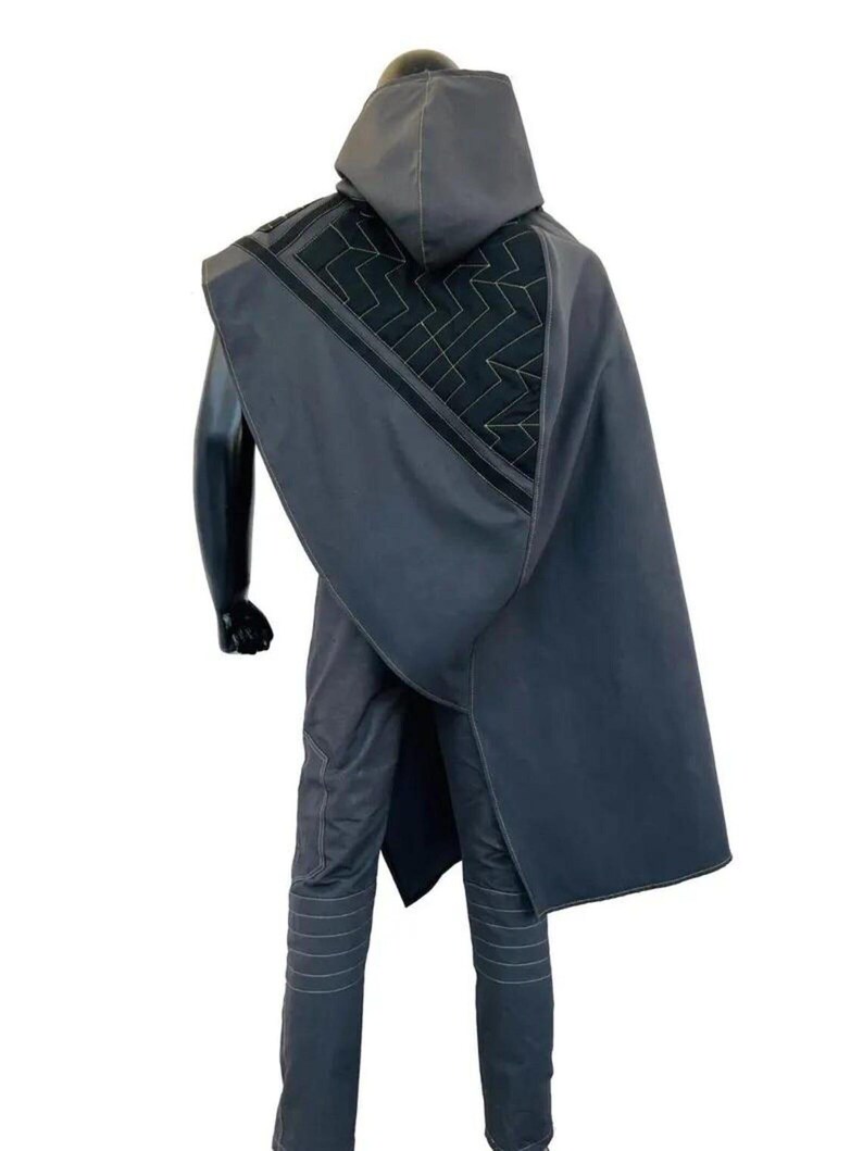 May include: A dark gray hooded cloak featuring a black triangular panel with a gold geometric zigzag pattern on the back. The cloak is worn over matching dark gray trousers with horizontal stitched detailing on the legs, presented on a mannequin.