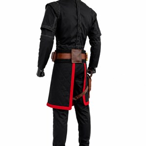 May include: A black costume featuring a high-collared jacket with white stitching, a brown leather utility belt with pouches, and a black quilted tunic with red trim. The outfit includes black trousers and black gloves, worn by a mannequin.