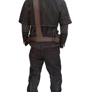 Op de afbeelding: Een zwarte outfit in tactische stijl bestaande uit een jack met korte mouwen en een bijpassende broek met witte contraststiksels. Het jack heeft geometrische patronen op de mouwen en een bruine utility-riem met schouderband wordt erover gedragen.