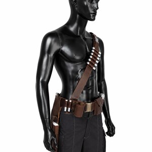May include: A brown leather bandolier and utility belt set worn over the torso and waist. The bandolier features a series of silver-colored cylindrical cartridges. The belt includes multiple pouches, loops, and a metallic buckle closure.
