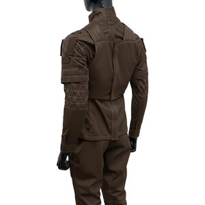 Pu&ograve; includere: Un completo composto da giacca e pantaloni in stile tattico color marrone scuro. La giacca presenta un colletto alto, pannelli strutturati sulle spalle e un motivo geometrico a triangoli cuciti sugli avambracci. Il capo presenta cuciture chiare visibili.