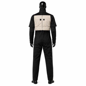 May include: A black jumpsuit featuring a high collar and short sleeves with white geometric stitching patterns. A beige, rectangular, padded vest is worn over the torso, secured with a central vertical zip and two small black square accents.