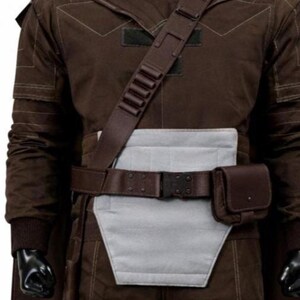 May include: A dark brown long-sleeved jacket with a light gray rectangular abdominal panel, a dark brown utility belt with a side pouch, and a matching brown shoulder strap featuring five small cylindrical loops across the chest area.