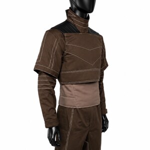 Puede incluir: Una chaqueta marr&oacute;n de manga larga con cuello alto, que presenta costuras blancas, paneles negros en los hombros y un dise&ntilde;o superpuesto corto. La chaqueta se combina con pantalones marrones a juego que tambi&eacute;n tienen costuras blancas.