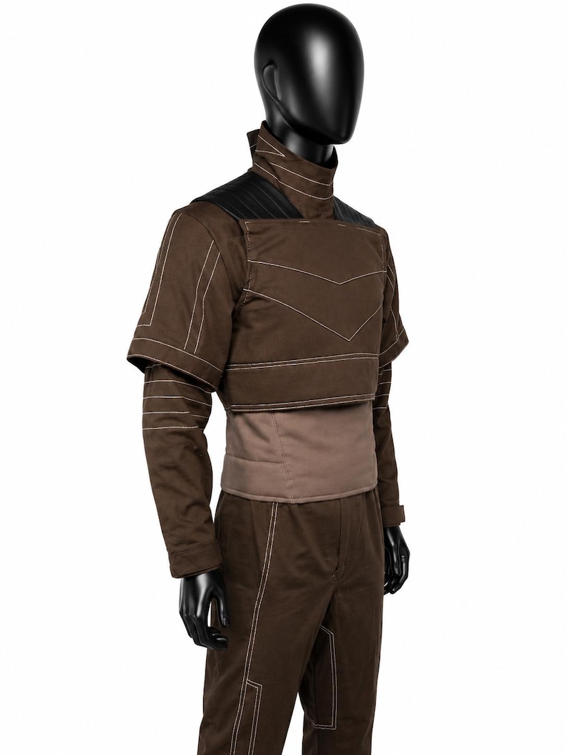 Puede incluir: Una chaqueta marr&oacute;n de manga larga con cuello alto, que presenta costuras blancas, paneles negros en los hombros y un dise&ntilde;o superpuesto corto. La chaqueta se combina con pantalones marrones a juego que tambi&eacute;n tienen costuras blancas.