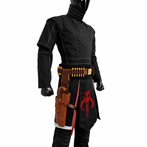 May include: A black costume featuring a high-neck tunic with white stitching, matching trousers, and a brown leather belt with gold-colored ammunition loops and a holster. A black apron with a red skull emblem hangs over the front of the outfit.