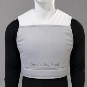 K&ouml;nnte beinhalten: Ein Brustschutz mit einer hellgrauen Vorderseite und dem gestickten Text Sewns By Soul in dunkelgrauem Garn. Das Kleidungsst&uuml;ck verf&uuml;gt &uuml;ber wei&szlig;e, gepolsterte Schultergurte und wird &uuml;ber einem schwarzen Langarmshirt auf einem Torso getragen.